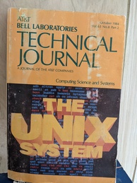 AT&T Bell Laboratories Technical Journal book cover. Orange book with a graphic showing large text announcing THE UNIX SYSTEM on the bottom half