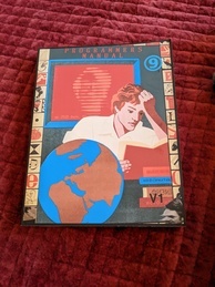Cover of the 9front Programmer's Manual V1. Features a person intently reading a book while several more books are in a pile waiting to be read and a globe sits next to the reader. A red screen is behind the reader with the text 'up 2920 days' with the rest of the message obscured. The 9front logo is in the upper-right corner, and the indicator V1 is in the bottom-right. 