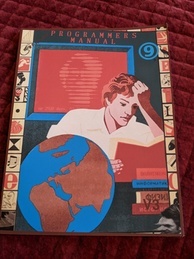 Cover of the 9front Programmer's Manual V3. Features a person intently reading a book while several more books are in a pile waiting to be read and a globe sits next to the reader. A red screen is behind the reader with the text 'up 2920 days' with the rest of the message obscured. The 9front logo is in the upper-right corner, and the indicator V3 is in the bottom-right.