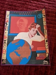 Cover of the 9front Programmer's Manual V5. Features a person intently reading a book while several more books are in a pile waiting to be read and a globe sits next to the reader. A red screen is behind the reader with the text 'up 2920 days' with the rest of the message obscured. The 9front logo is in the upper-right corner, and the indicator V5 is in the bottom-right.