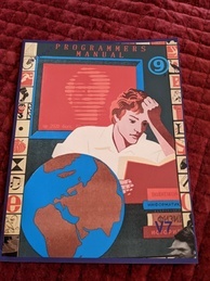 Cover of the 9front Programmer's Manual V7. Features a person intently reading a book while several more books are in a pile waiting to be read and a globe sits next to the reader. A red screen is behind the reader with the text 'up 2920 days' with the rest of the message obscured. The 9front logo is in the upper-right corner, and the indicator V7 is in the bottom-right.