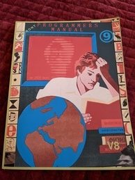 Cover of the 9front Programmer's Manual V8. Features a person intently reading a book while several more books are in a pile waiting to be read and a globe sits next to the reader. A red screen is behind the reader with the text 'up 2920 days' with the rest of the message obscured. The 9front logo is in the upper-right corner, and the indicator V8 is in the bottom-right.