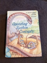 Operating System Concepts, seventh edition. Features a mother dinosaur watching over a nest of three juvenile dinosaurs. One is using a PDA, one is using a laptop, and one is using some kind of audio player and is wearing headphones.