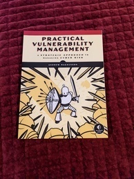 Cover of the Practical Vulnerability Management book. Features a drawing of a humanoid robot wielding a sword and a shield that is riddled with blocked arrows. The robot appears to be defending against a massive incoming force of armor-clad creatures wielding swords.