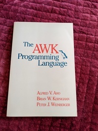 Cover of The AWK Programming Language book. Beige background with the title of the book in blue and white. Features a small drawing of an auk bird to the right of the title.
