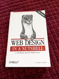 Cover of the Web Design in a Nutshell O'Reilly book, 2nd edition. Features an image of a least weasel popping up from behind the logo, its head, shoulders and forelimbs are visible. There is a banner announcing the 2nd edition in the upper-right hand corner