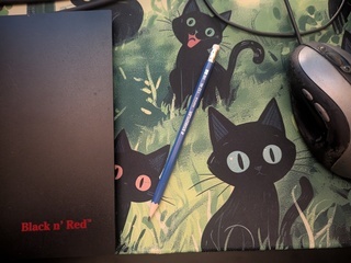 A Staedtler Norica pencil sitting on a mat covered with a bunch of cartoon cats