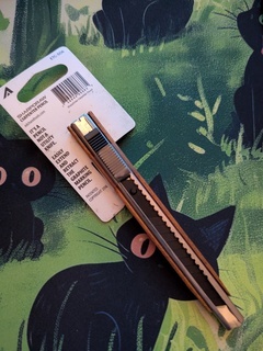SHARPDRAW® carpenter pencil in its packaging. The packaging is flipped over so you can more easily see the 'blade' and how the pencil is almost exactly like a utility knife except for the graphite blade